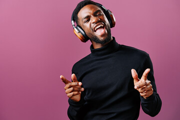 Joyful Black man wearing headphones enjoying music against a pink background, showcasing emotions and style through fashion