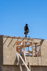 Framing contractor standing roof of new home construction with a nail gun, sunny blue sky as background, workman on job site
