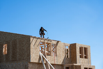 Framing contractor standing roof of new home construction with a nail gun untangling air compressor...