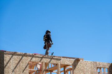 Framing contractor standing roof of new home construction with a nail gun, sunny blue sky as background, workman on job site
