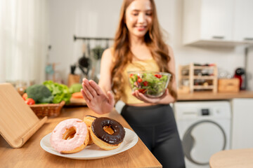 Asian beautiful woman rejecting junk food and eating salad in kitchen. 