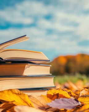 Stack of books resting on autumn leaves outdoors in natural light with blue sky and blurred background reading concept