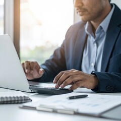 Fototapeta premium A professional man in a tailored suit sits at a sleek desk, intently focused on his laptop, surrounded by modern office decor and soft lighting.