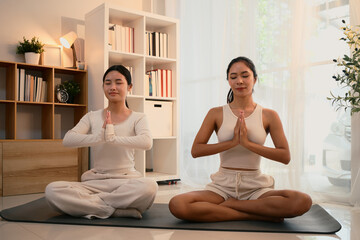 Calm and focused mother and daughter practicing yoga together in a peaceful indoor