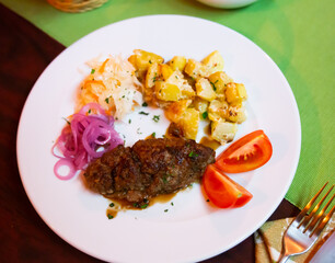 Plate with a meat dish lula-kebab, stewed potatoes, pickled cabbage, onions and slices of fresh tomato.