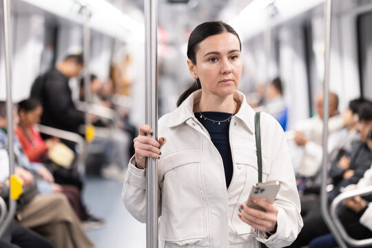Portrait of woman using smartphone while traveling in subway car - Powered by Adobe