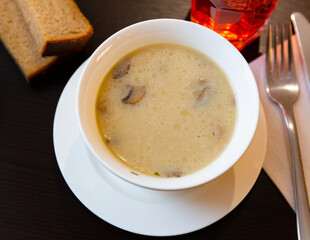 Portion of fresh mushroom soup served in soup bowl with serving pieces and brea