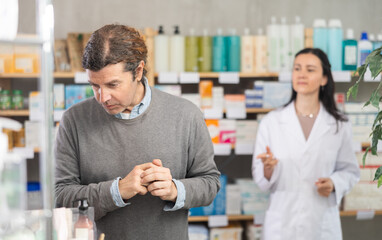 Obraz premium Male customer looking for something in a drugstore. Female pharmacist offers him medicines