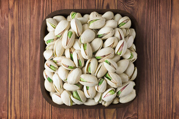 shelled pistachio nuts in square plate on wooden table background. vegetarian organic food for healthy diet.