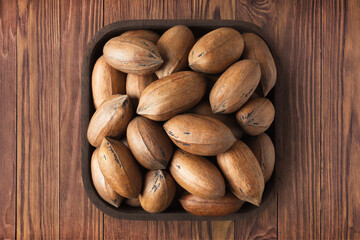 Obraz premium shelled pecan nuts raw in square plate on wooden table background. vegetarian organic food for healthy diet.
