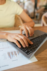 Hands typing on a laptop with business charts on a table, showcasing a productive work environment.