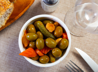 Assorted large olives served in bowl with pieces of pickled vegetables..