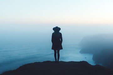 Woman stands at the edge of a cliff overlooking a hazy ocean at dawn
