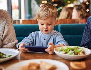 Smartphones are the new babysitters—while parents enjoy their meal, kids dive into screens. A modern family moment at a restaurant.