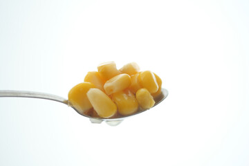 Close-up of corn kernels on a spoon against a bright background