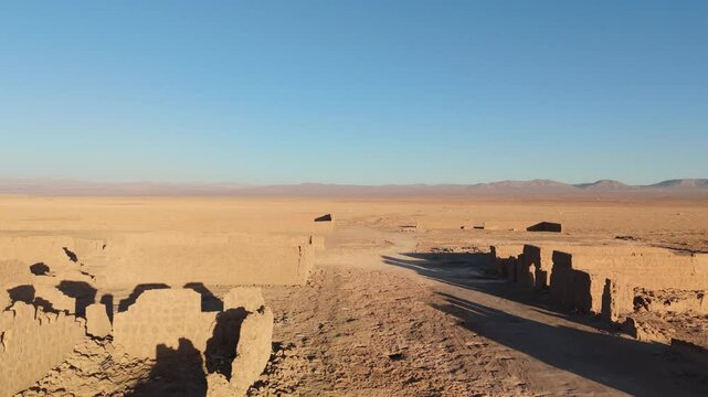 Smooth drone footage flying sideways over the ruins of an abandoned saltpeter refinery in the heart of the Atacama Desert, Chile. Wide view of adobe structures,