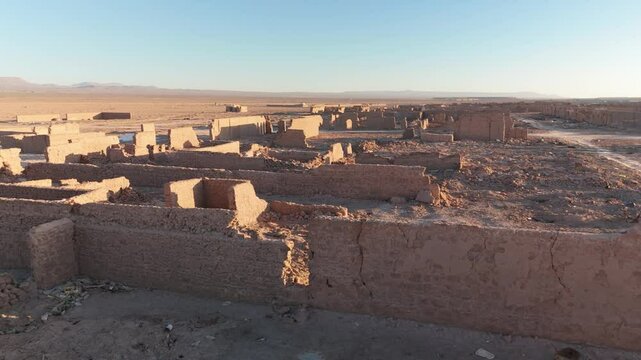 Close-up drone shot of the ruined adobe facades of a former saltpeter works, curved towards the sunset.