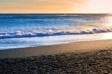 Golden sun light on black sand beach and ocean blue water on evening time in vik , Island.