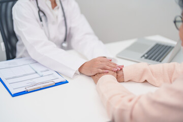 doctor holding hands with elderly female patient, showing empathy and support during a medical...