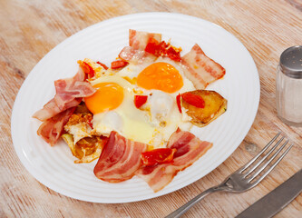 Bacon with fried potato and egg served on plate on wooden table