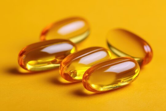 Close up of yellow softgels containing fish oil omega 3s EPA DHA and vitamins D3 E and A on a yellow background