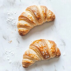 Two golden croissants on a marble surface