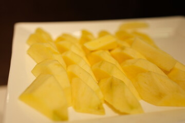 Ripe yellow mango flesh, cut into jagged slices, placed on a white plate against a multicolored background