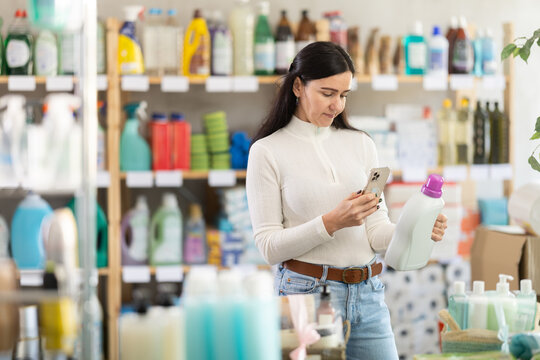 Adult woman scans the barcode of a detergent package on a mobile camera. Customer uses online banking for contactless payment for goods in a supermarket