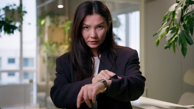 Asian serious business woman looking at camera businesswoman pointing wristwatch wait meeting check time hurry deadline punctuality in office Chinese Korean Japanese girl appointment hand clock timing