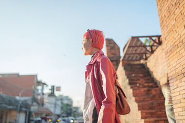 Fototapeta premium Gen z girl leather fashion with punk Asian woman tourist of local city Southeast Asia travel trendy pink hairstyle young female punk traveler walking around in town