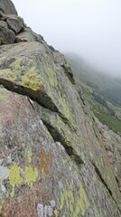 Fototapeta premium Granite slope with lichen in the Pyrenees mountains on a foggy day close up view of rock texture and green valley in background