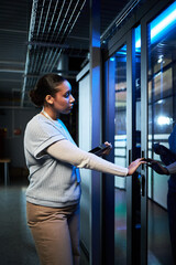 Woman standing in server room entrance holding keycard and scanning it for access. Focused...