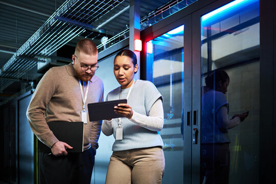Two professionals discussing data security strategies in modern server room with tablet. Collaboration between team members in a high-technology environment