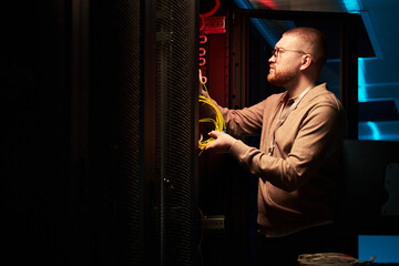 Technician working in server room attaching network cables. Background includes server racks and...