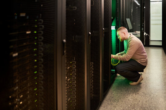 Technician configuring server equipment in data center. Focus on network setup and hardware adjustments within server racks. Neon glowing lights adding visual appeal