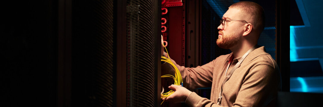 Technician adjusting network cables in data center amidst rows of servers and electronic equipment creating an atmosphere of modern digital workspace