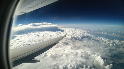 Airplane wing above a vast expanse of fluffy clouds, viewed from the window.  A clear blue sky is visible above