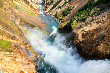Mist from the powerful Lower Falls in Yellowstone National Park creates a vivid rainbow over the Grand Canyon of the Yellowstone, adding color to the rugged landscape. UNESCO world heritage in Wyoming