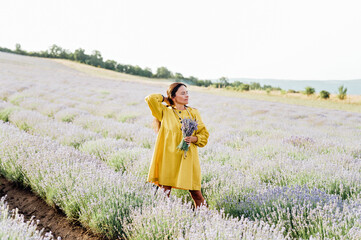woman in yellow dress stands in lavender field, gently holding bouquet of lavender flowers. She...