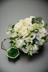 white roses in a bouquet for the bride on her wedding day next to a glass box with gold rings lying on a natural grass mat, for the bride and groom on their wedding day