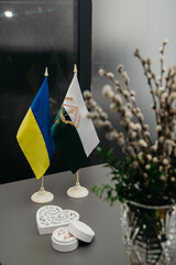 Wedding rings in a white box lie on the table next to the flags of Ukraine and Poltava as well as fresh wildflowers in a vase