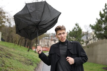 Man with broken umbrella fighting wind under rain outdoors