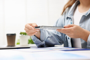 Woman taking photo of document using scanning app on smartphone at desk in office, closeup. Space for text