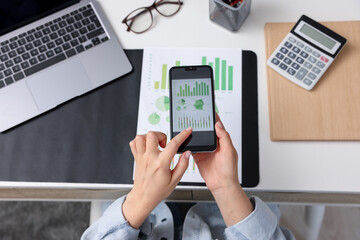 Woman taking photo of document using scanning app on smartphone at desk in office, above view