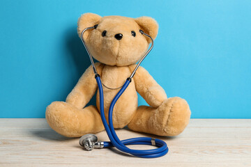 Pediatrics concept. Teddy bear with stethoscope on wooden table against light blue background