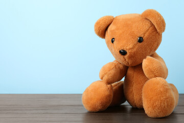 Obraz premium Cute teddy bear on wooden table against light blue background. Space for text