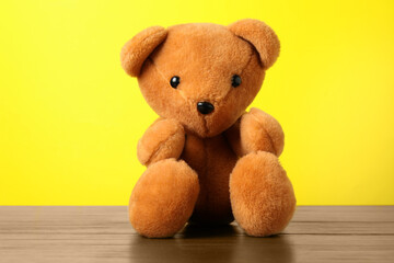 Fototapeta premium Cute teddy bear on wooden table against yellow background