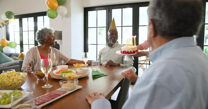 Group of happy senior multiracial, white and black male and female friends blowing candles at a birt