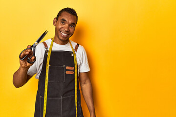 African American tailor with tools, yellow studio, happy, smiling and cheerful.