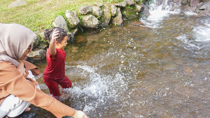 A daughter playing in a river with red clothes with her mother